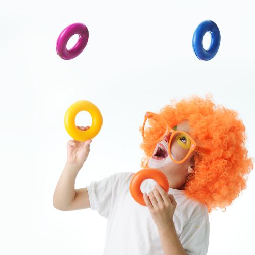 Un enfant avec une perruque et un maquillage de clown jongle avec des anneaux de couleurs