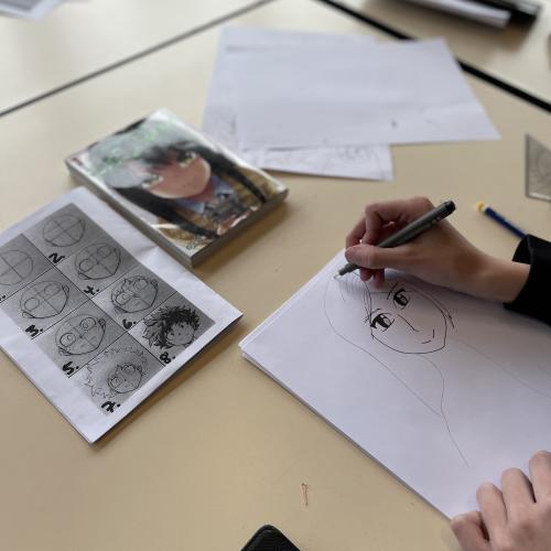 Un participant à l'atelier en train de dessiner un portrait dans le style manga avec, devant lui, des livres en exemple