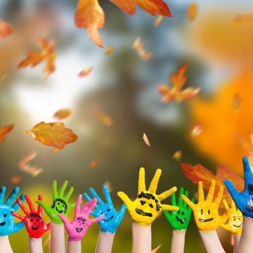 Des mains d'enfants peintes de différentes couleurs et représentant différentes émotions jetant des feuilles mortes en l'air