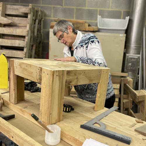 Une participante à l'atelier peaufine une petite table en bois réalisée à partir de palettes