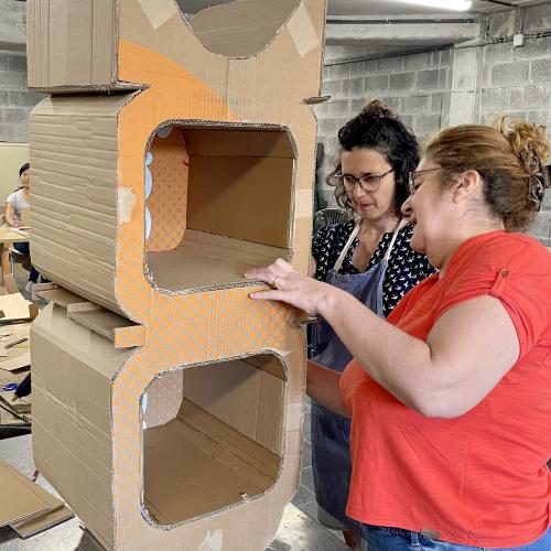 Lors d'un précédent stage, deux femmes en train de peaufiner un meuble en carton, du style étagère