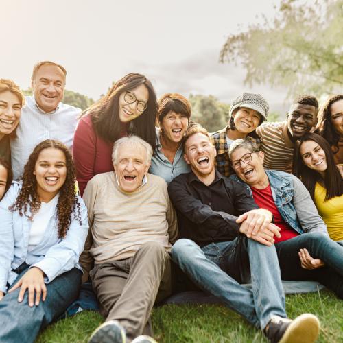 Un groupe de personnes de tous âges, assis par terre dans l'herbe, en train de rire