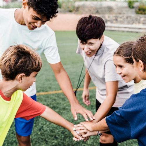 Un petit groupe d'enfants et de jeunes sur un terrain de sport extérieur, en train de se taper dans la main pour s'encourager