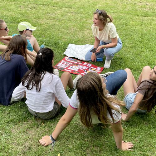Un petit groupe de jeunes ados apprenent une chanson en néerlandais assis dans l'herbe du parc de La Louve