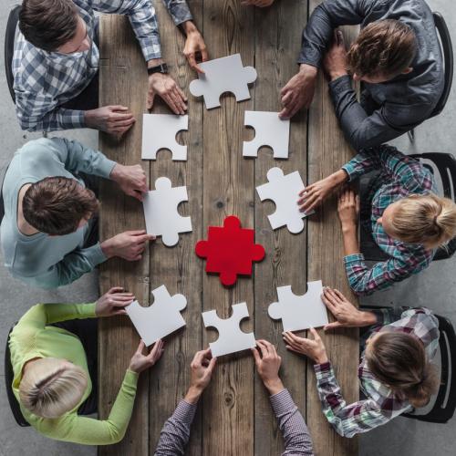 Vue en plongée sur une table autour de laquelle sont assises plusieurs personnes qui assemblent les pièces d'un puzzle