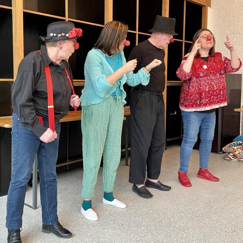 Un groupe de quatre personnes, hommes et femmes, en train d'interpréter un exercice de clown