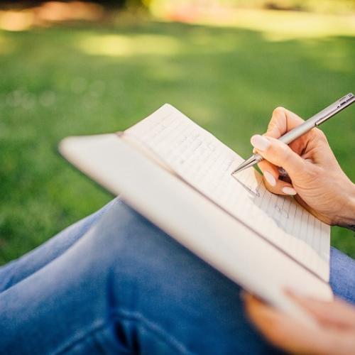 Une personne assise dans l'herbe écrit sur un cahier