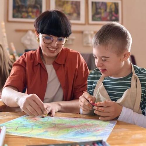 Une animatrice réalisant un dessin avec un enfant porteur de handicap