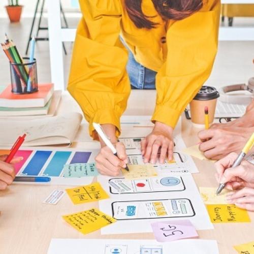 Un groupe de personnes autour d'une table, gros plan sur leurs mains en train d'assembler des documents colorés