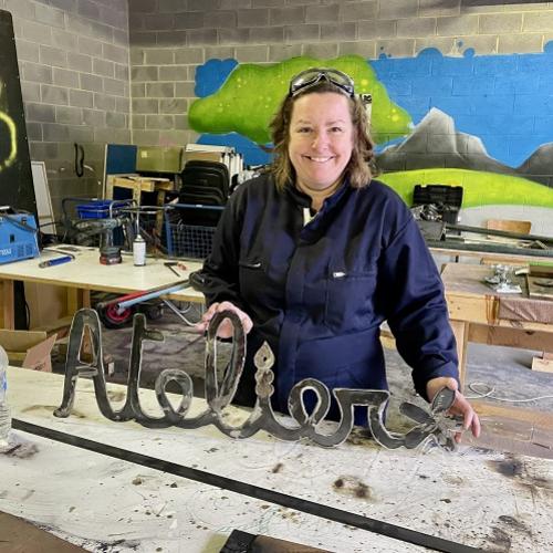 Une participante souriante présente sculpture de métal sous la forme du mot "atelier"