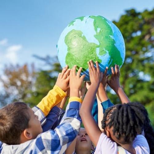 Un groupe d'enfants tient un ballon en forme de planète Terre au bout de leurs bras tendus