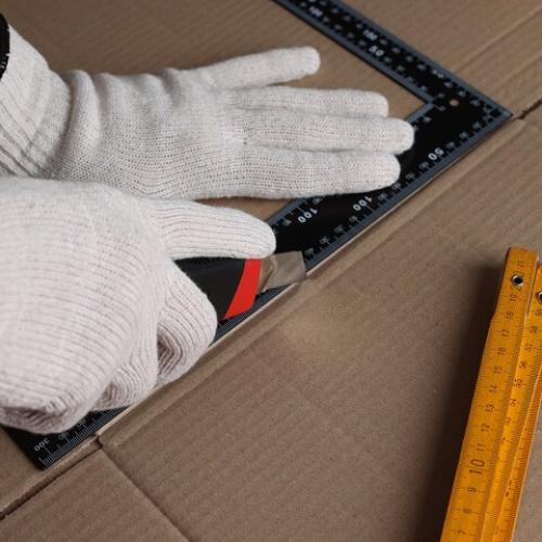 Des mains avec des gants de protection découpent du carton avec un cutter