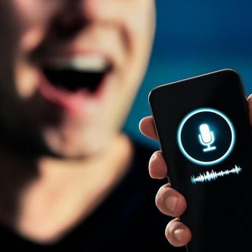 En avant-plan, un enregistreur prend le son. En arrière-plan, quelqu'un s'exprime