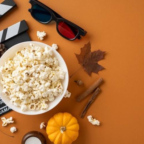 Sur un fond orange, un clap de tournage, un bol de pop-corn, des lunettes noires, une feuille d'érable et une citrouille