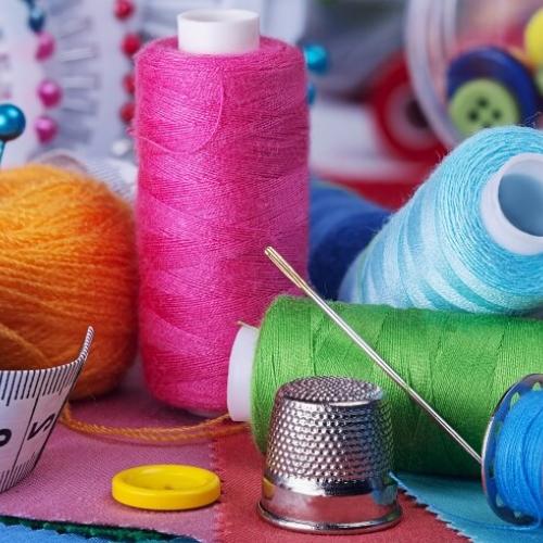 Un gros plan sur du matériel de couture (mètre ruban, bobines de fil multicolores, aiguilles, dé à coudre, ...)